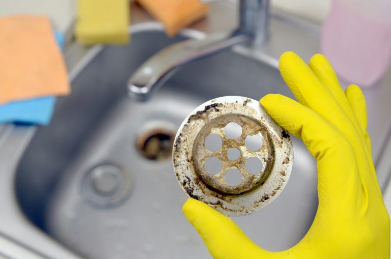 Cleaner in rubber gloves shows waste in the plughole protector of a kitchen sink