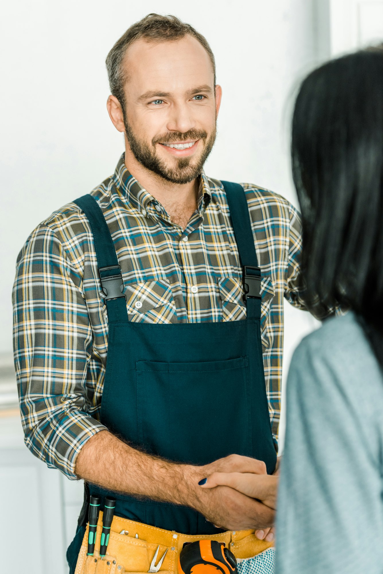 smiling handsome plumber and client shaking hands in kitchen