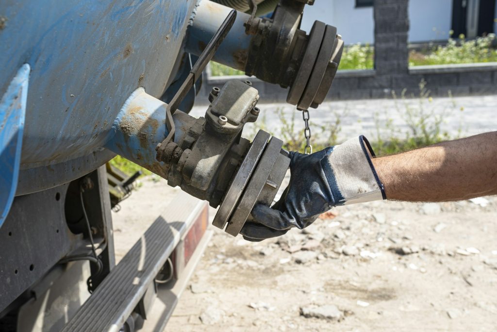 The man is disconnecting a 4 inch PVC suction hose to the flange fitting on the trucks tank.